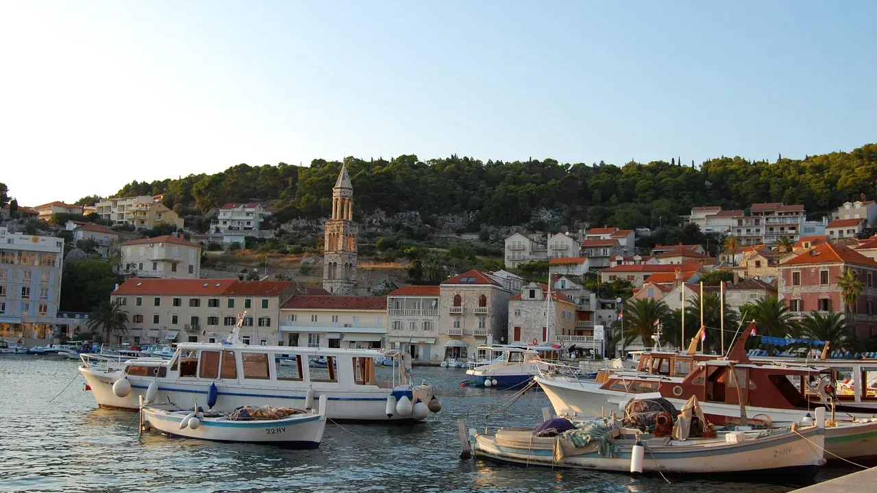 Wooden fishing boats moored in a Dalmatian harbour at golden hour, stone houses and a bell tower on the hillside