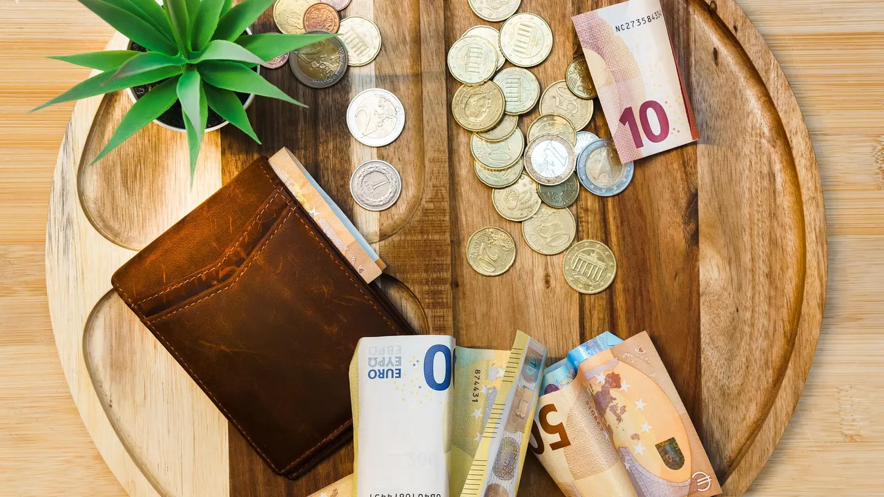 A wallet, euro banknotes, and coins laid out on a wooden tray