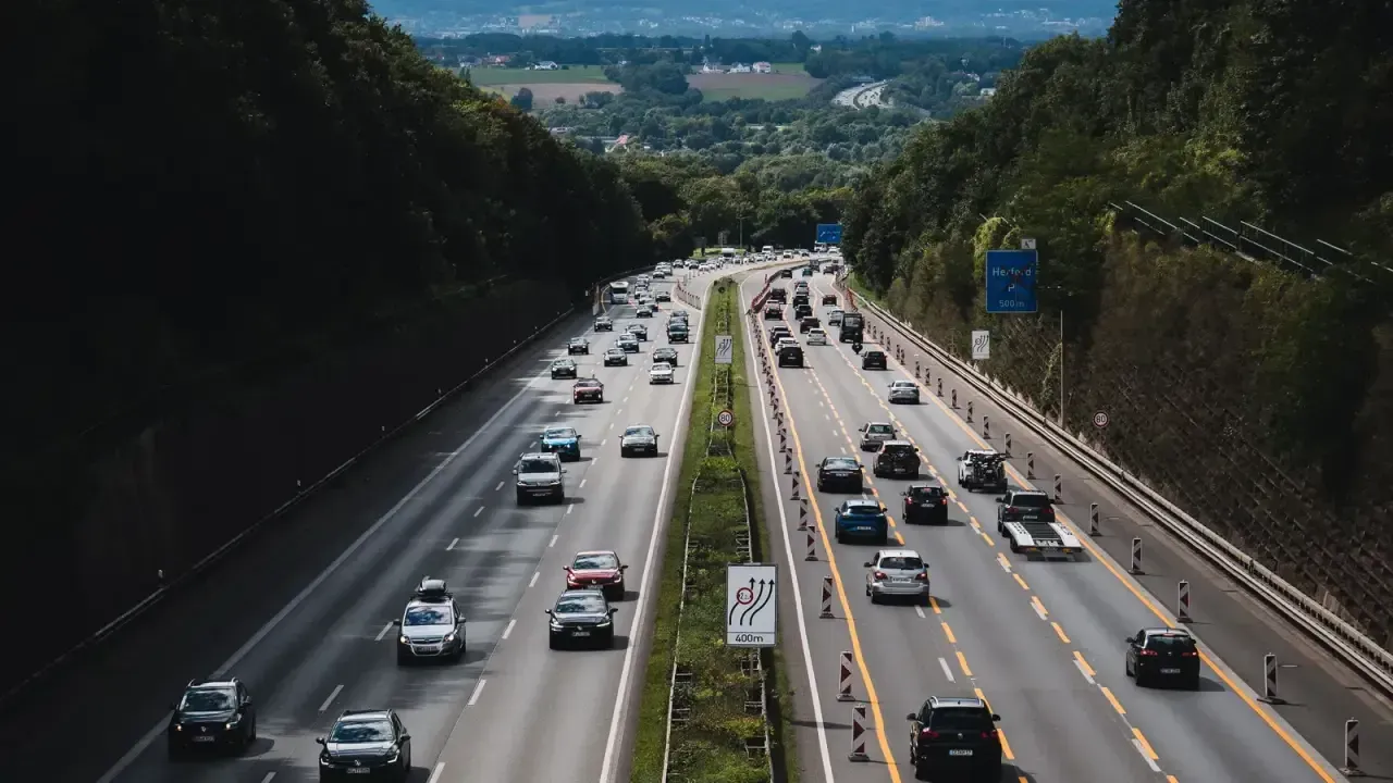 A multi-lane German Autobahn with heavy traffic cutting through forested hills near Herford